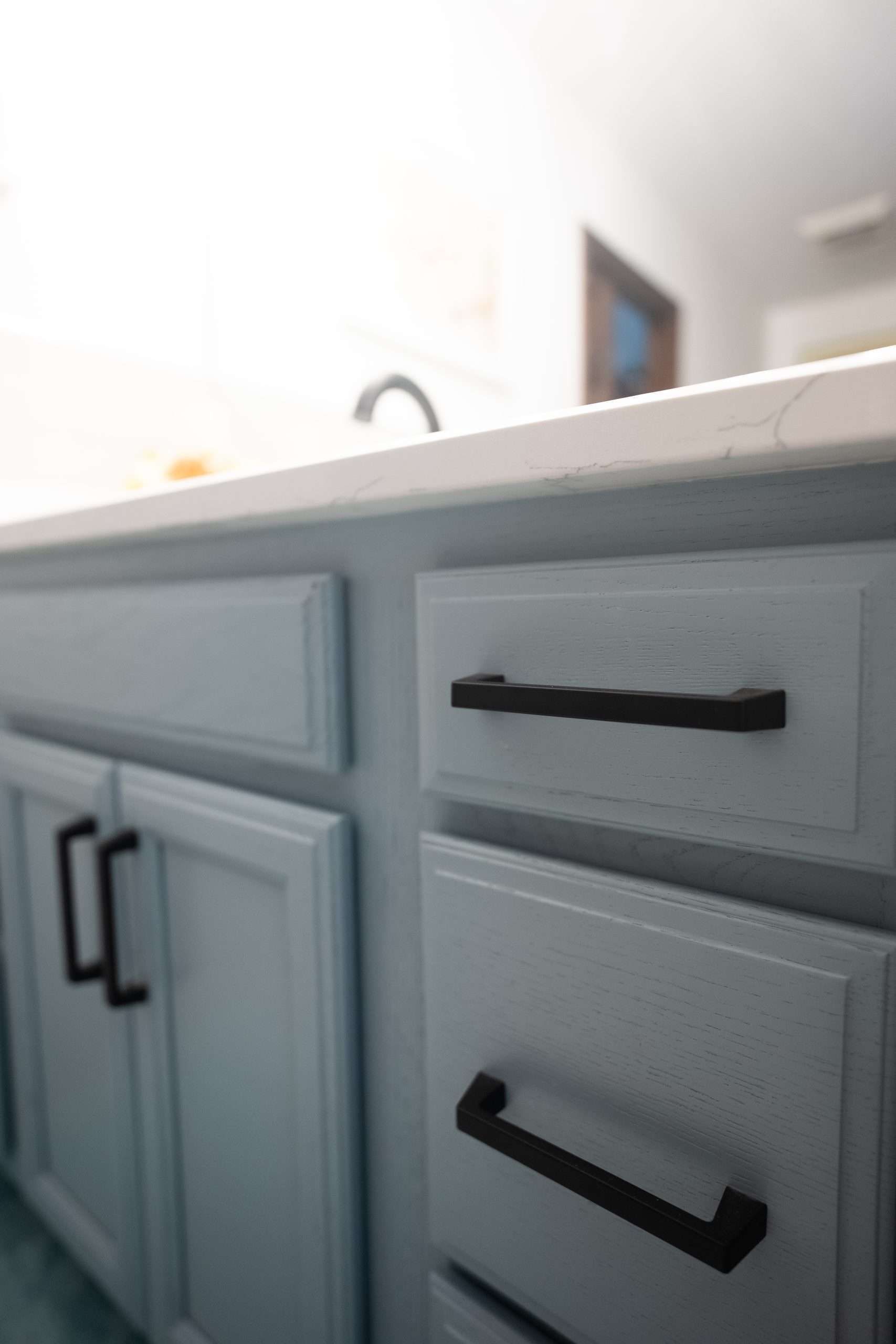 Light blue bathroom vanity with black handles and a white countertop under a sink.
