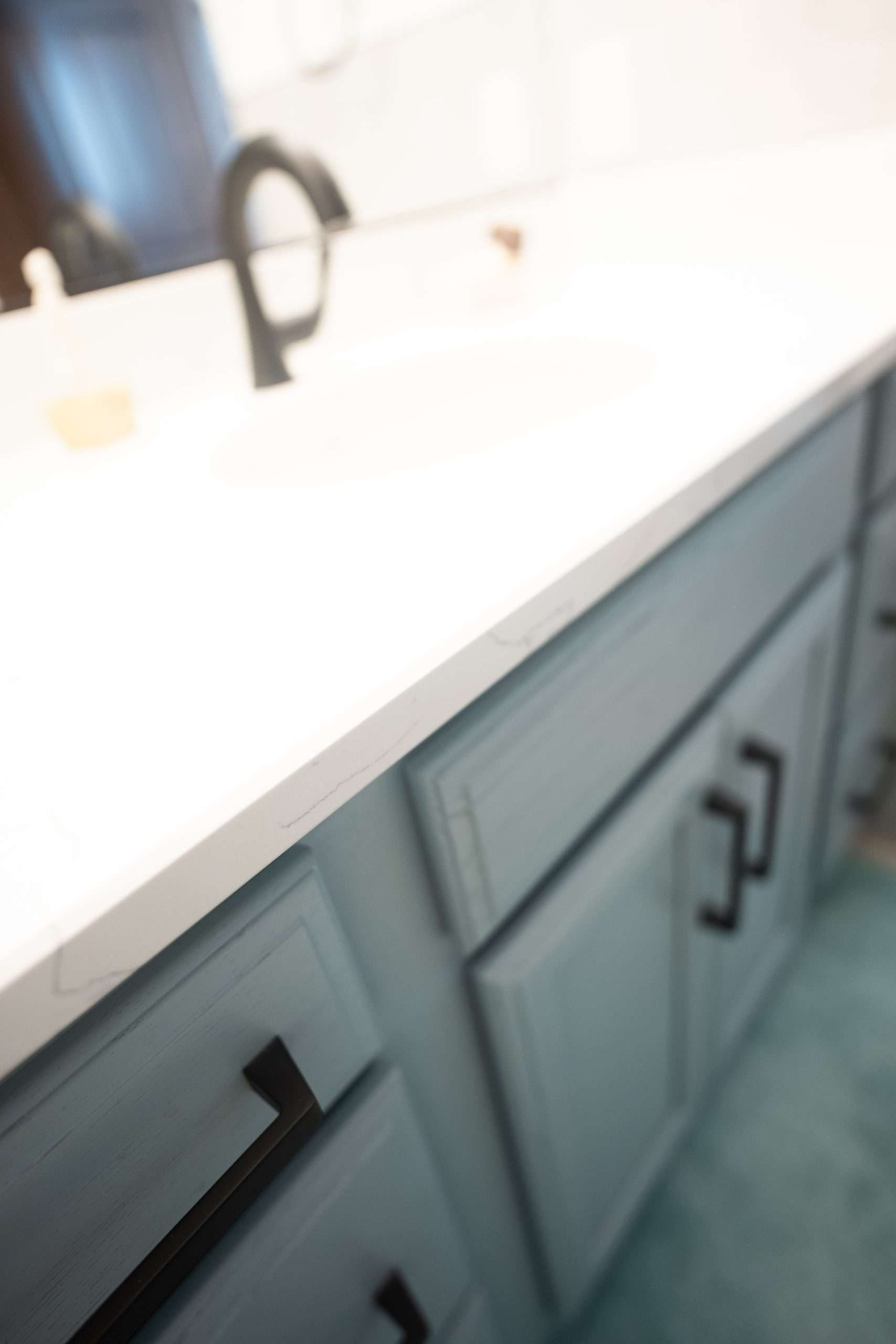 White kitchen countertop with gray cabinet drawers and black handles, seen at an angle.