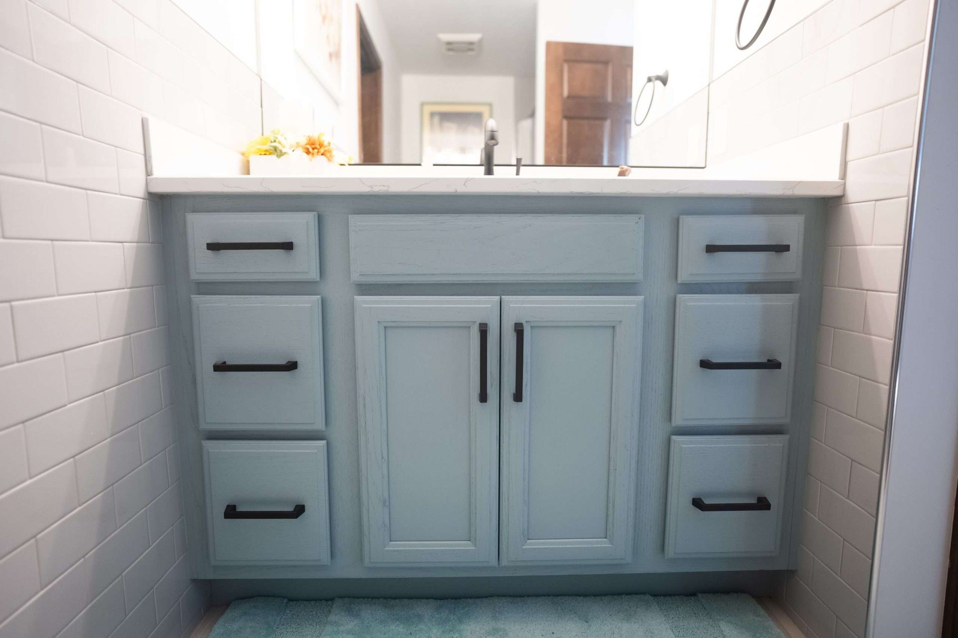 Light blue bathroom vanity with sink, drawers, and mirrored cabinet between white tiled walls.