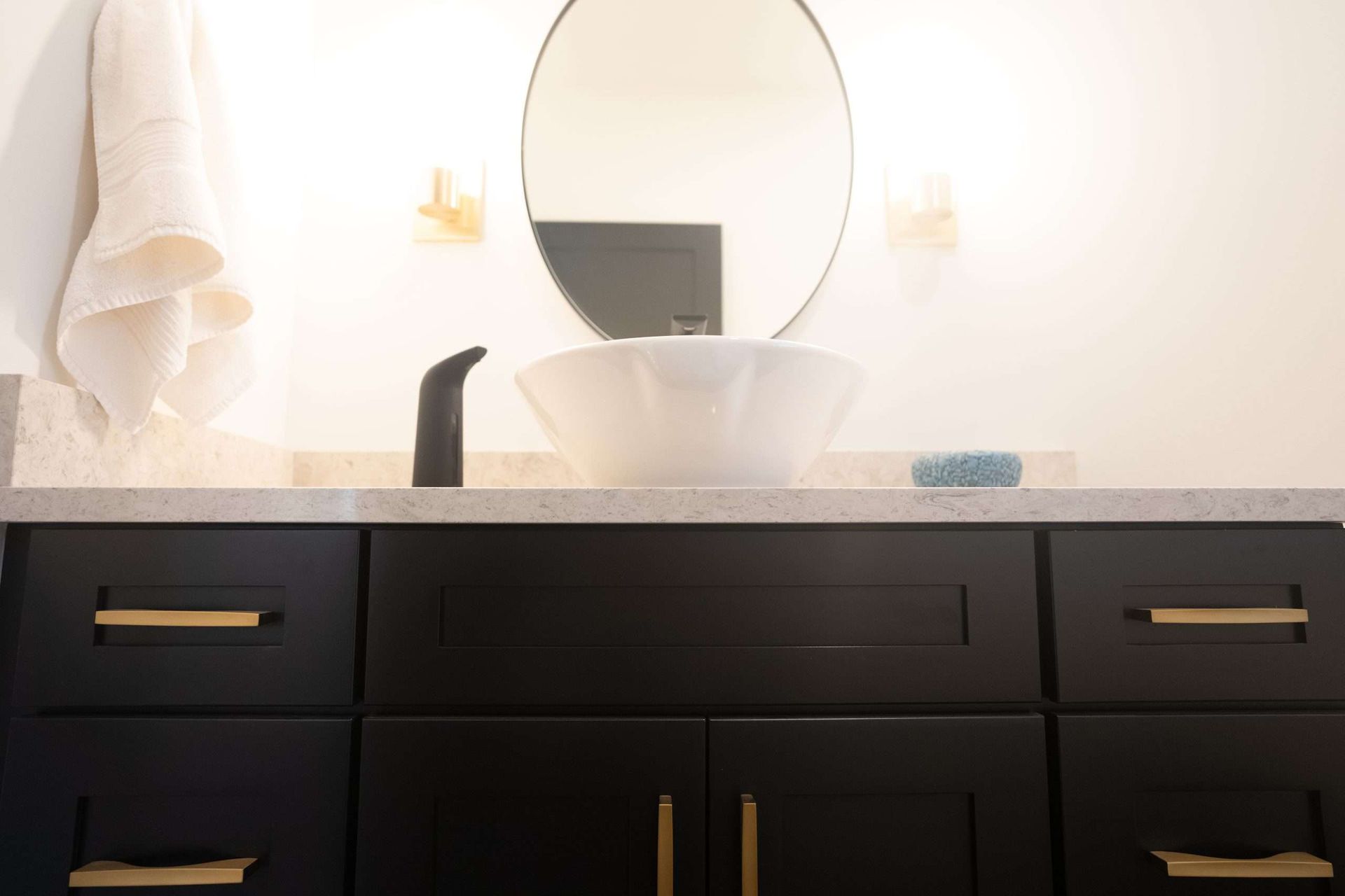 Modern bathroom vanity with black cabinets, brass handles, round mirror, and white vessel sink