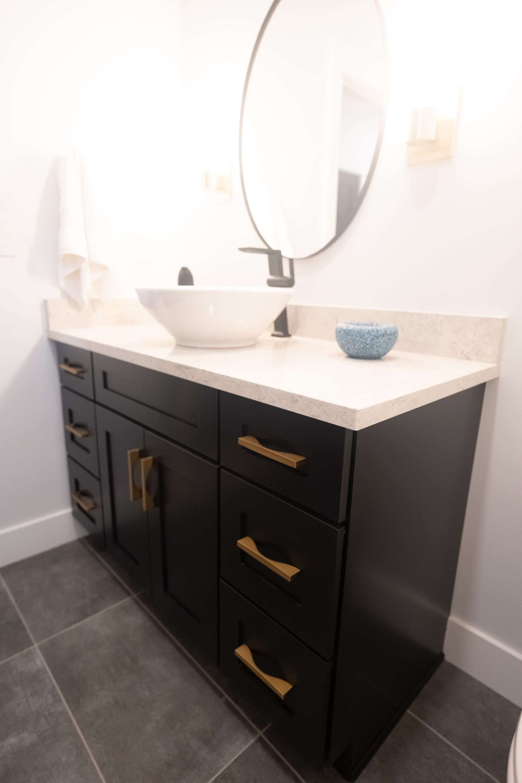 Small bathroom vanity with black cabinet, white countertop, round mirror, and vessel sink