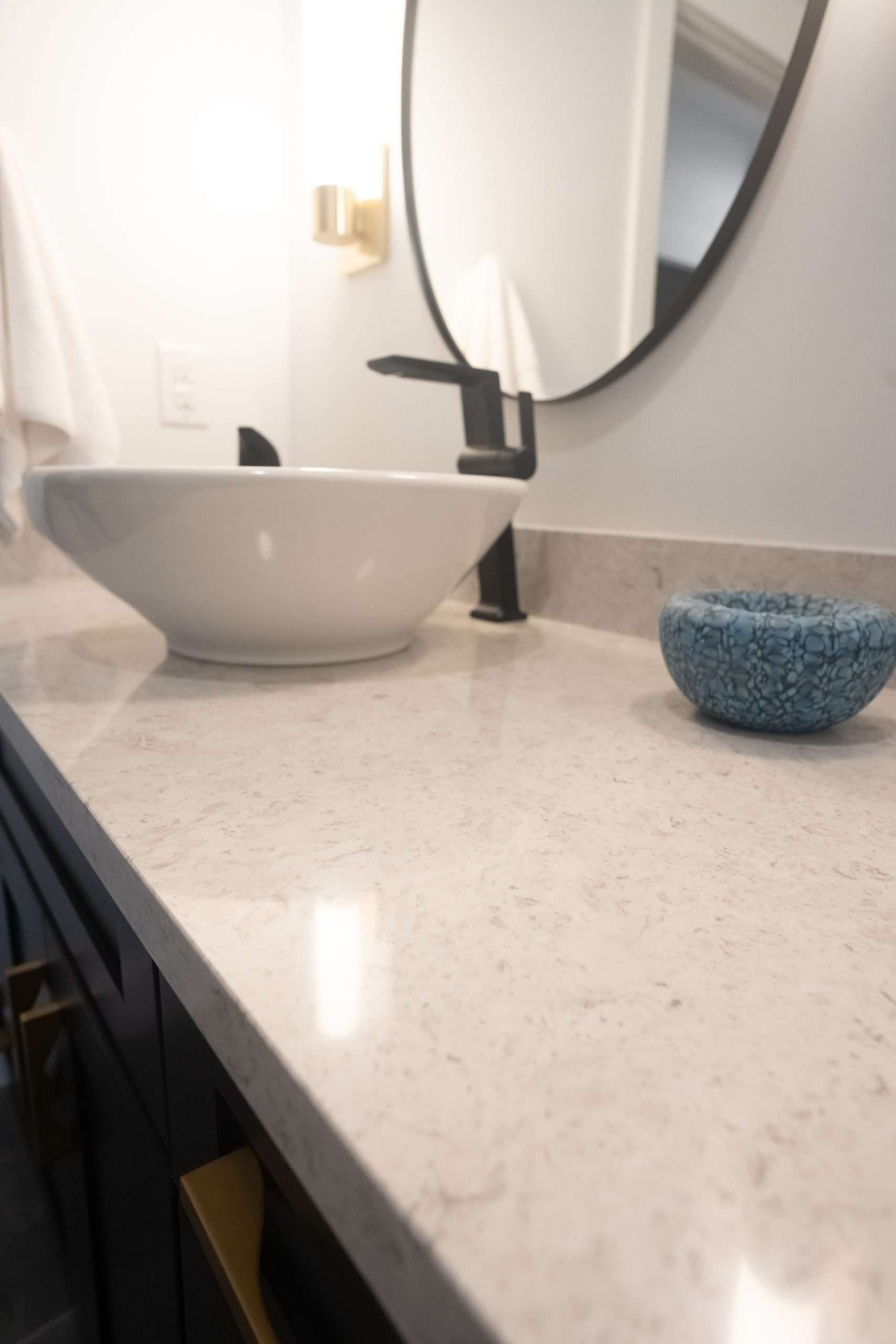 Modern bathroom vanity with vessel sink, black faucet, round mirror, and blue soap dish on speckled countertop