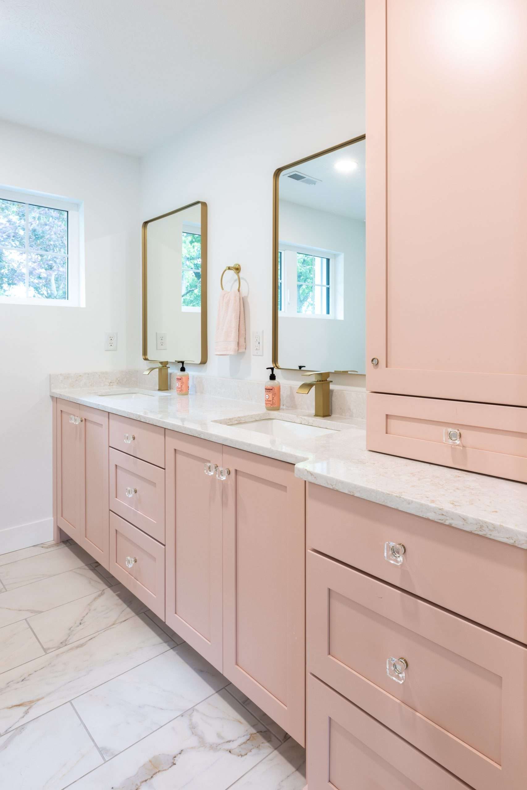 Modern bathroom vanity with pale pink cabinets, white countertop, mirrors, and marble tile floor.