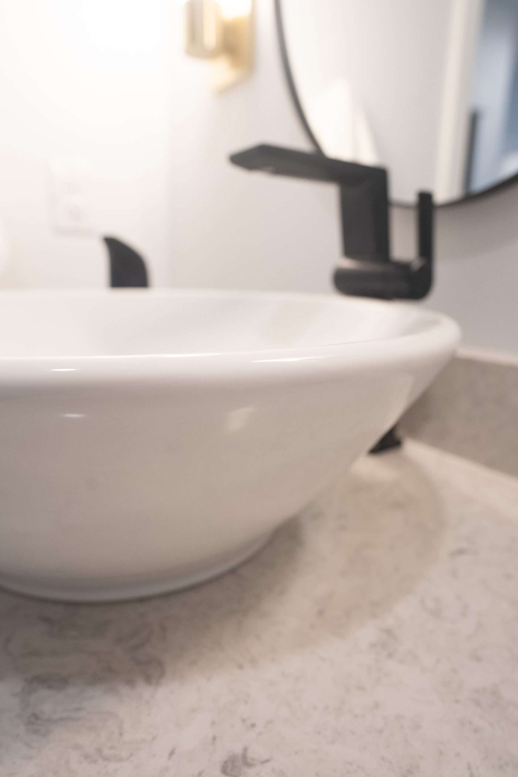 White bathroom sink with matte black faucet on a speckled countertop, close-up view