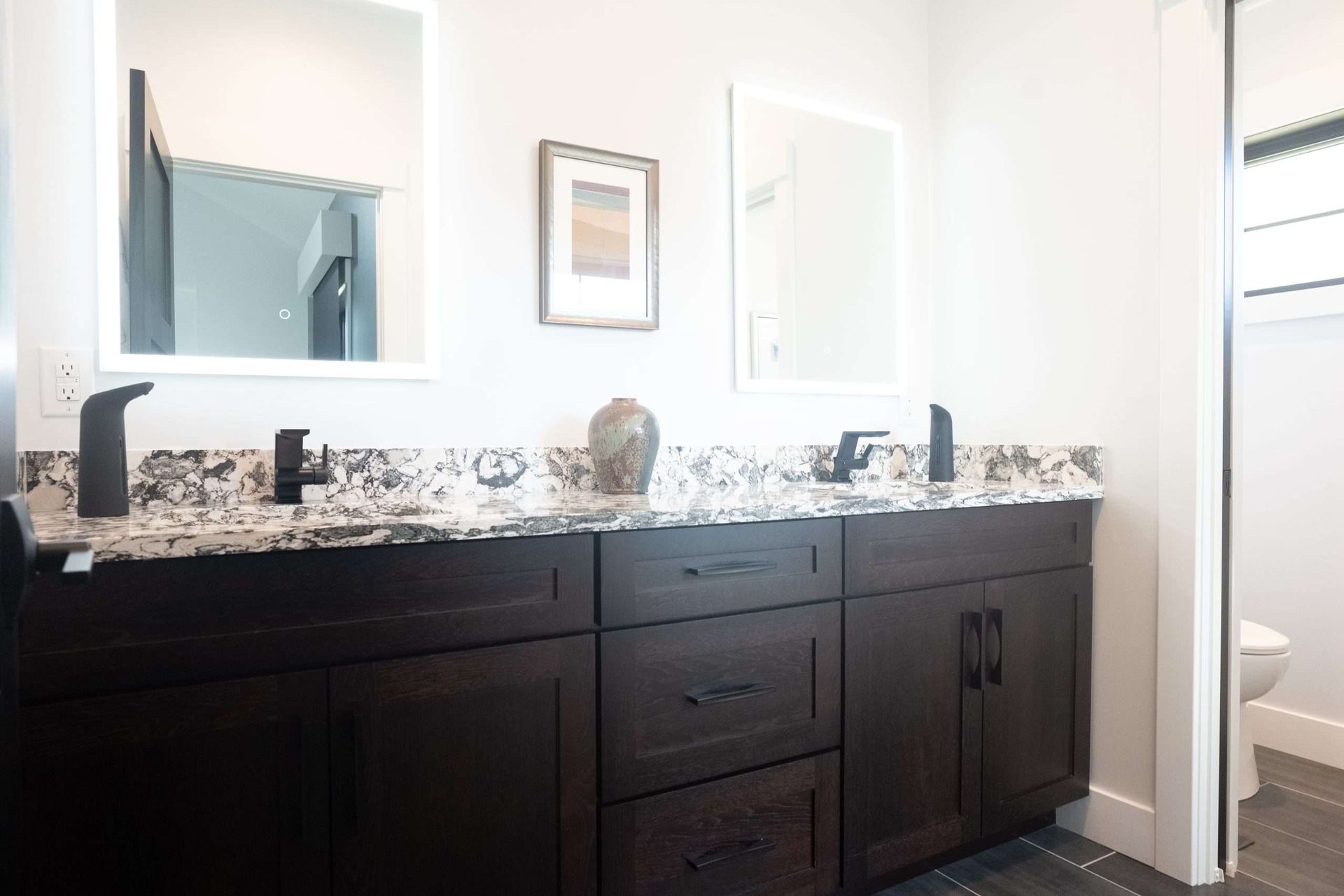 Dark wood bathroom vanity with granite countertop, sink, mirror, and toilet visible in the background.