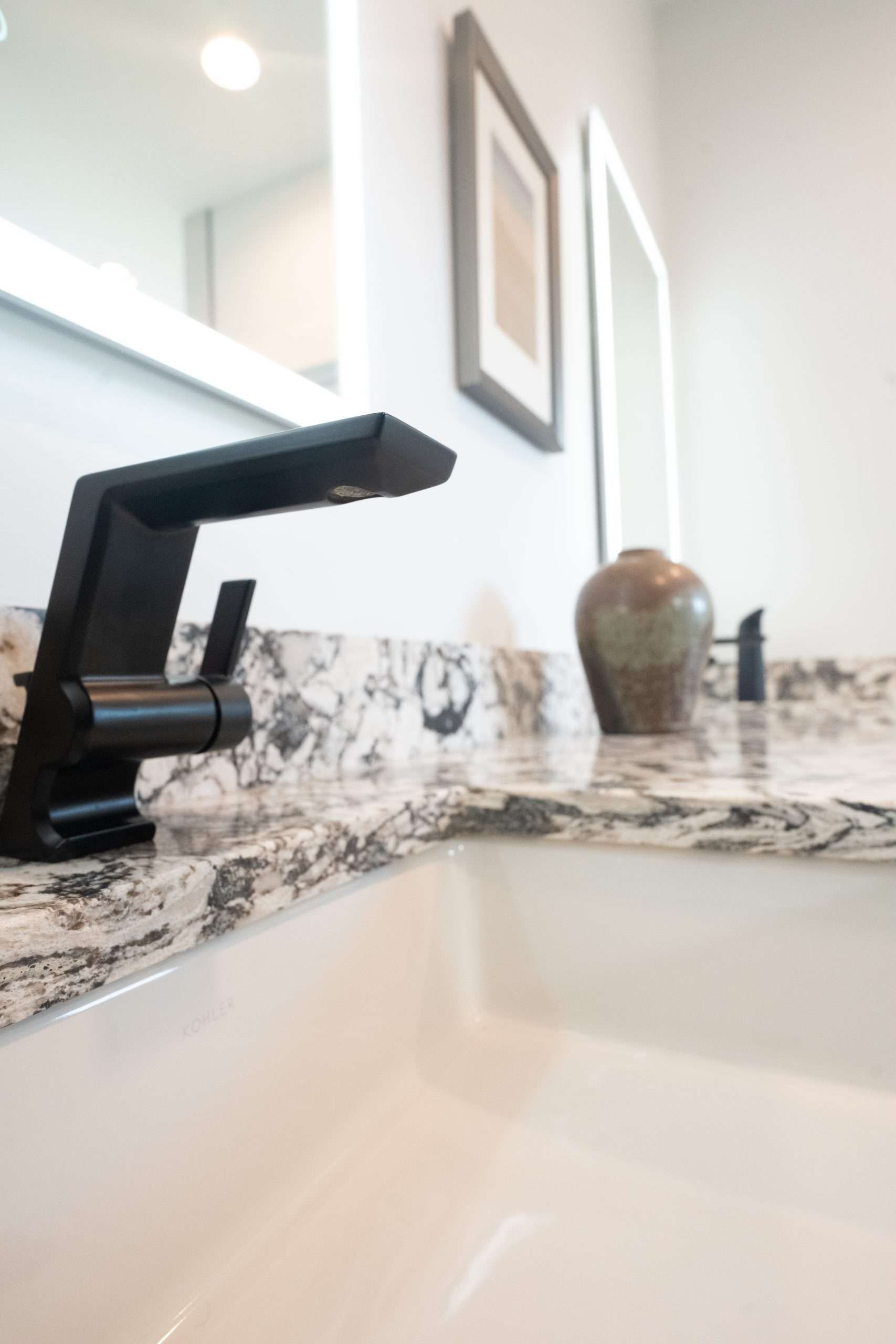 Modern bathroom sink with black faucet, marble countertop, and vase near a mirror