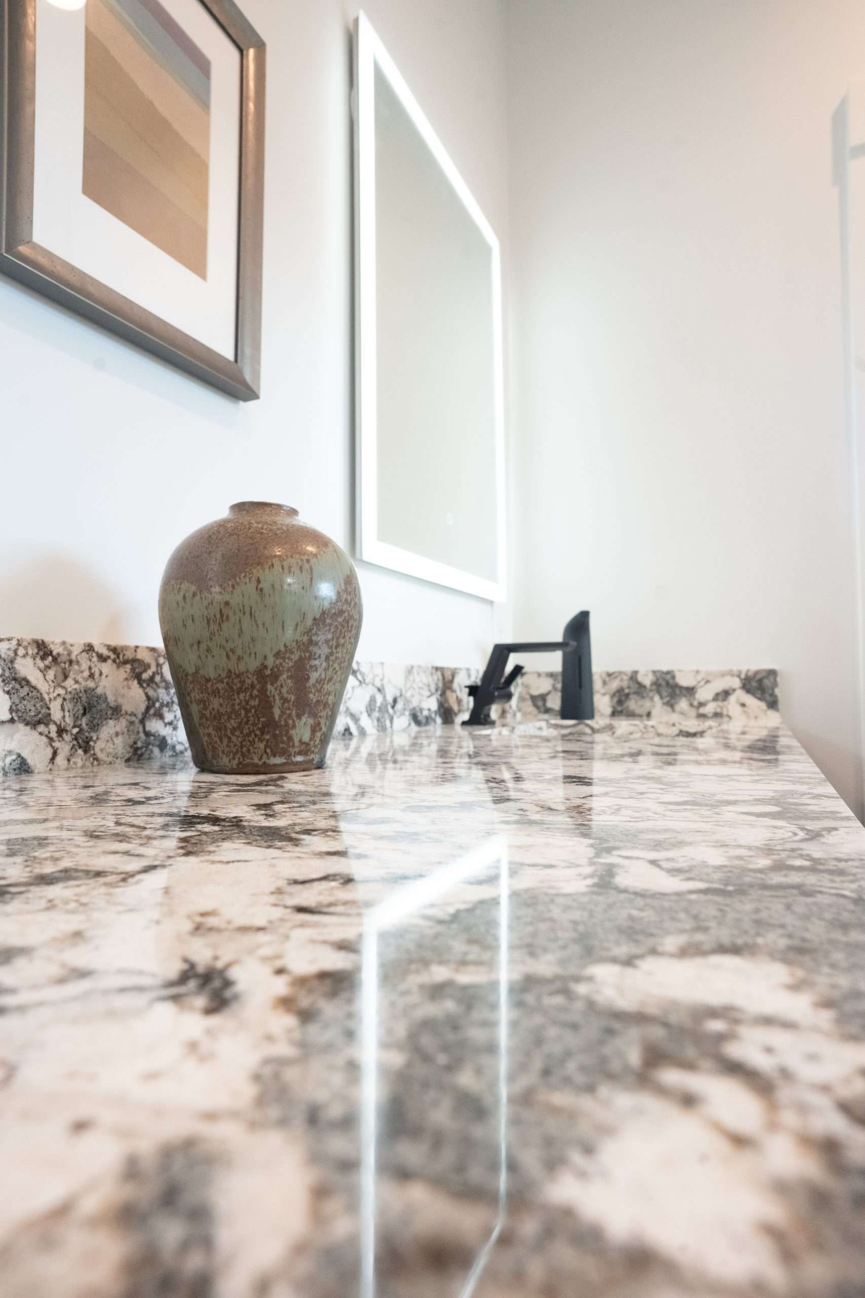Bathroom vanity with marble countertop, dark faucet, and decorative vase by a mirror