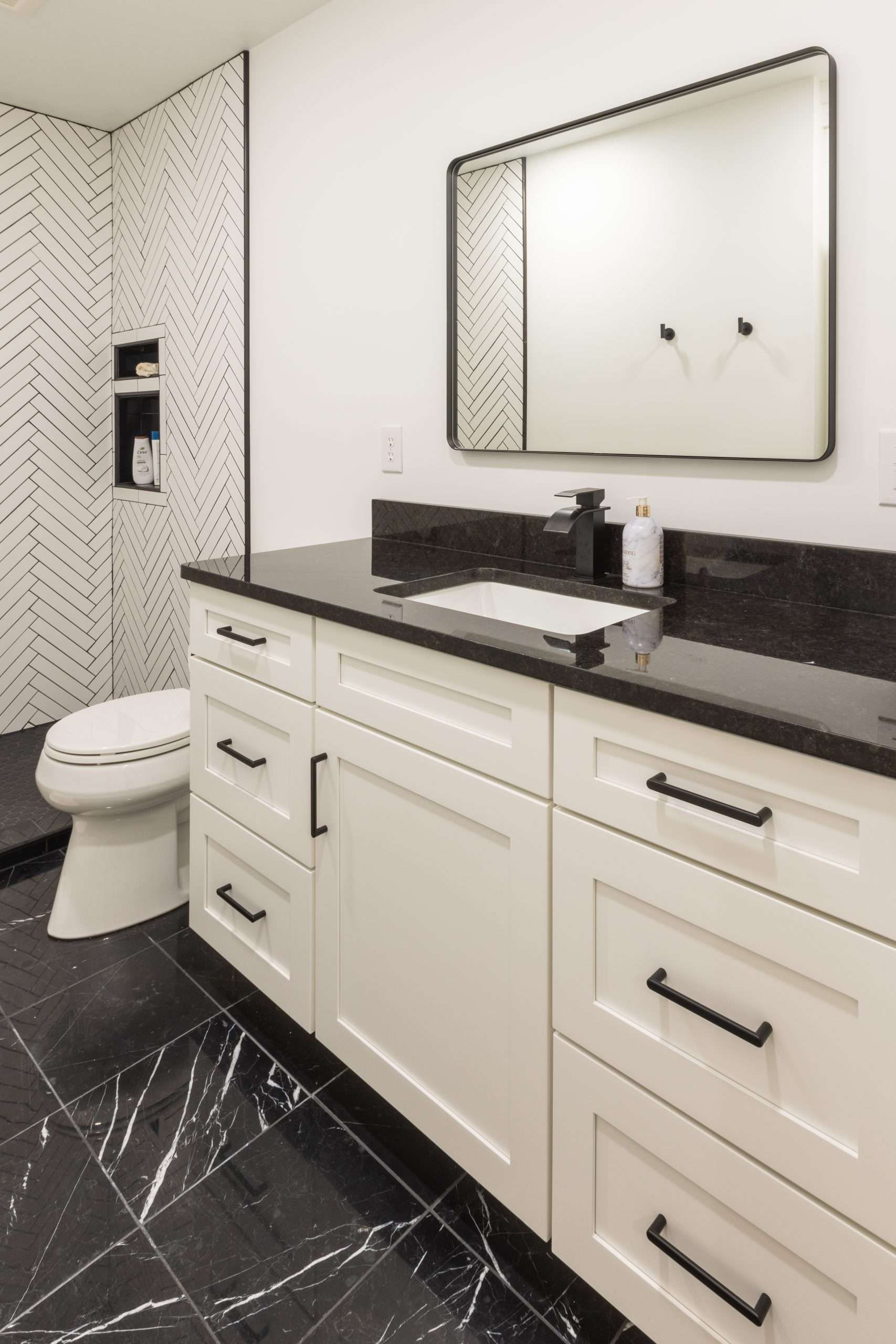 Modern bathroom with white vanity, black countertop, round mirror, and patterned shower tile