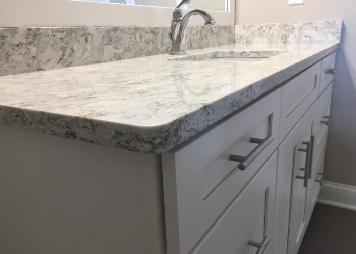 White bathroom vanity with marble countertop and sink faucet, shown in a bright modern bathroom.