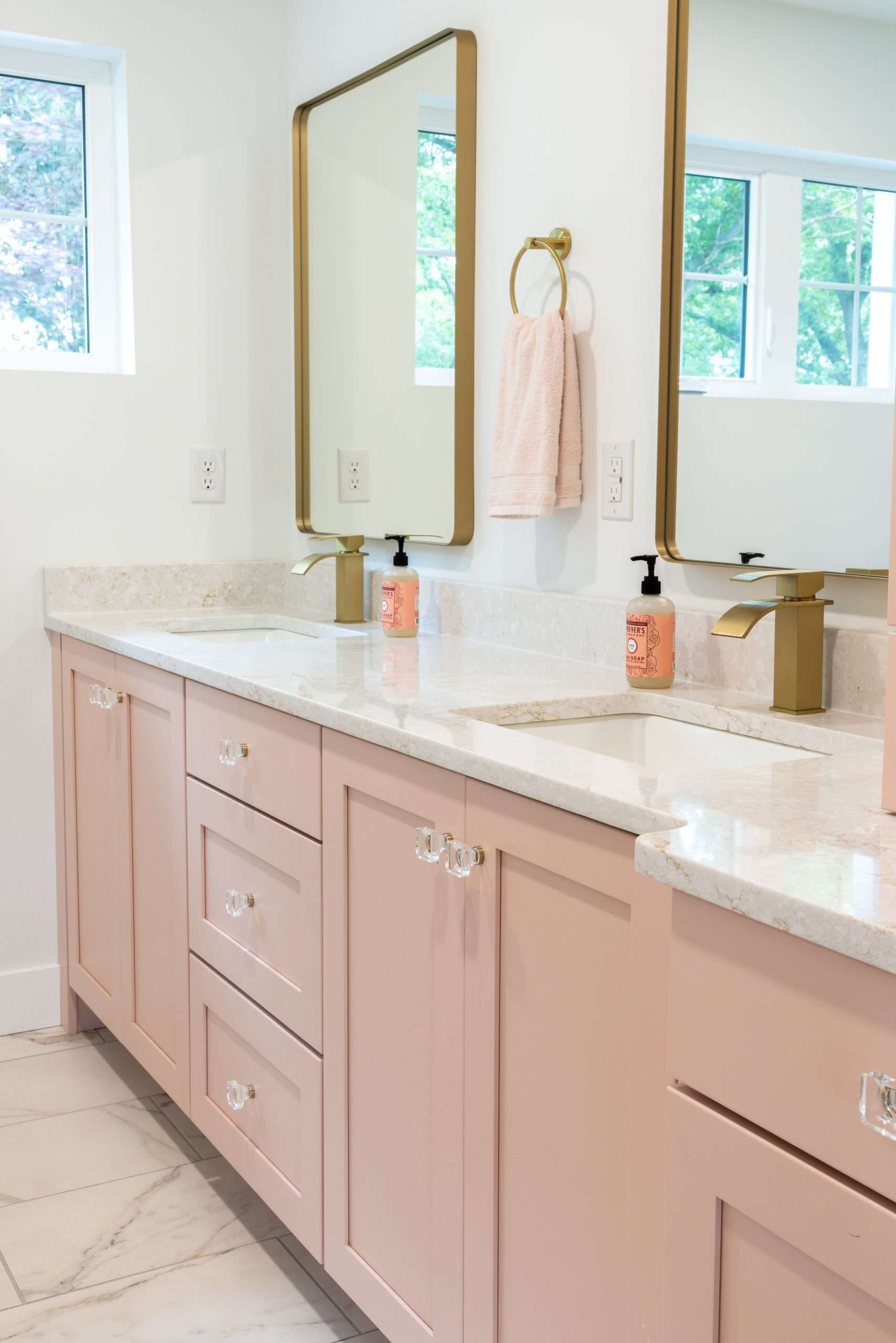 Pink bathroom vanity with white countertops, mirror, and natural light from windows