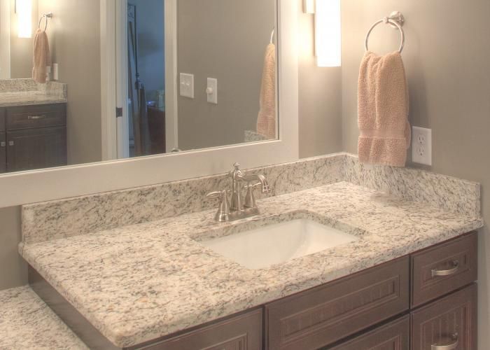 Bathroom vanity with speckled countertop, sink, mirror, and towel ring beside a lit wall sconce