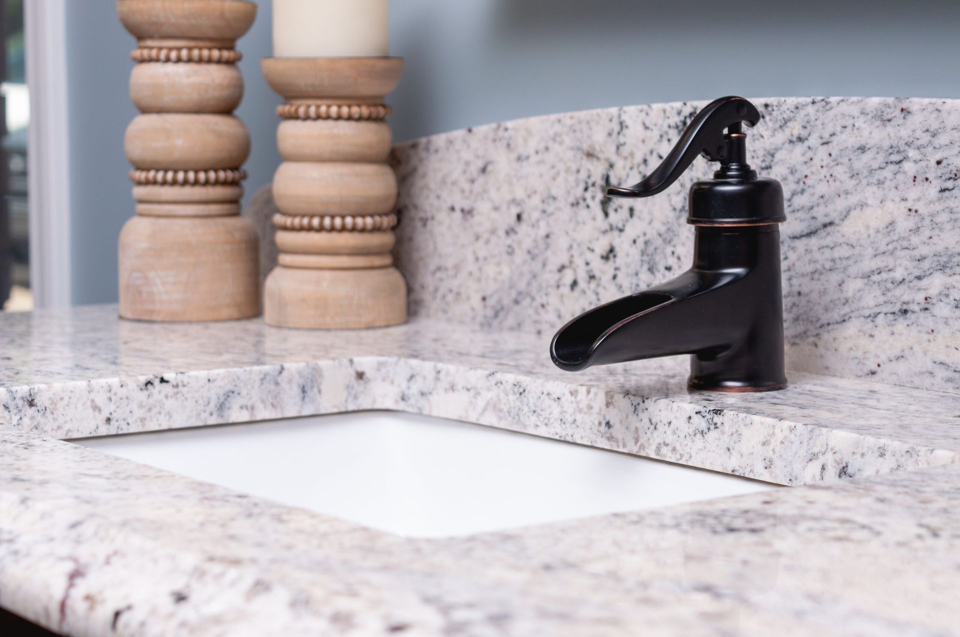 Modern bathroom sink with black faucet and marble countertop, white vessel basin, and decorative wooden accents