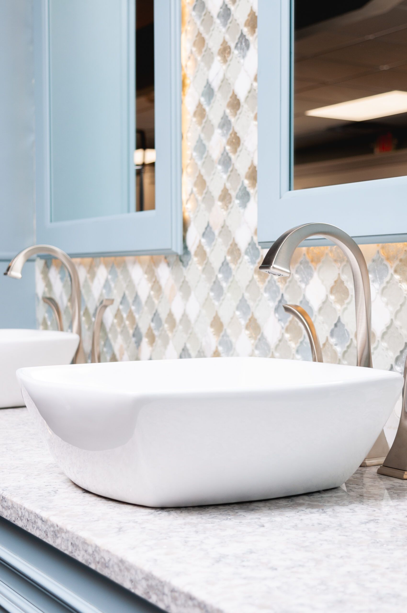 White vessel sink on a gray countertop with a chrome faucet and blue-framed mirror in a bathroom