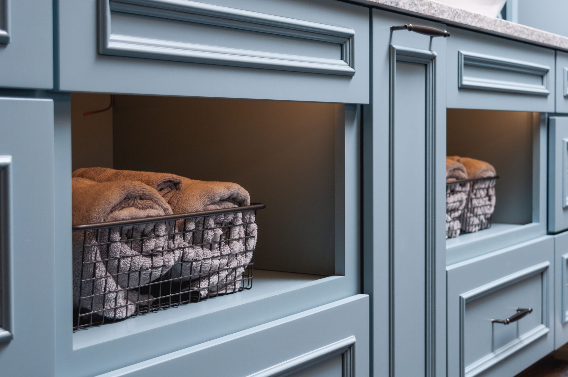 Wire baskets of bread inside a gray kitchen cabinet display.