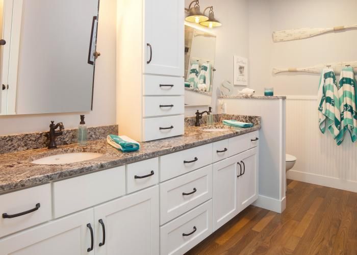Bright bathroom vanity with white cabinets, granite countertop, mirror, and teal towels beside a tub.