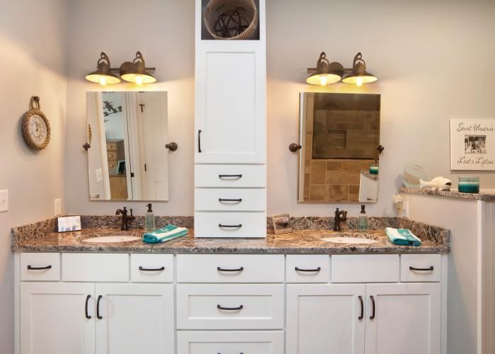 Bright bathroom vanity with double sinks, granite countertop, mirrors, and wall sconces above white cabinets