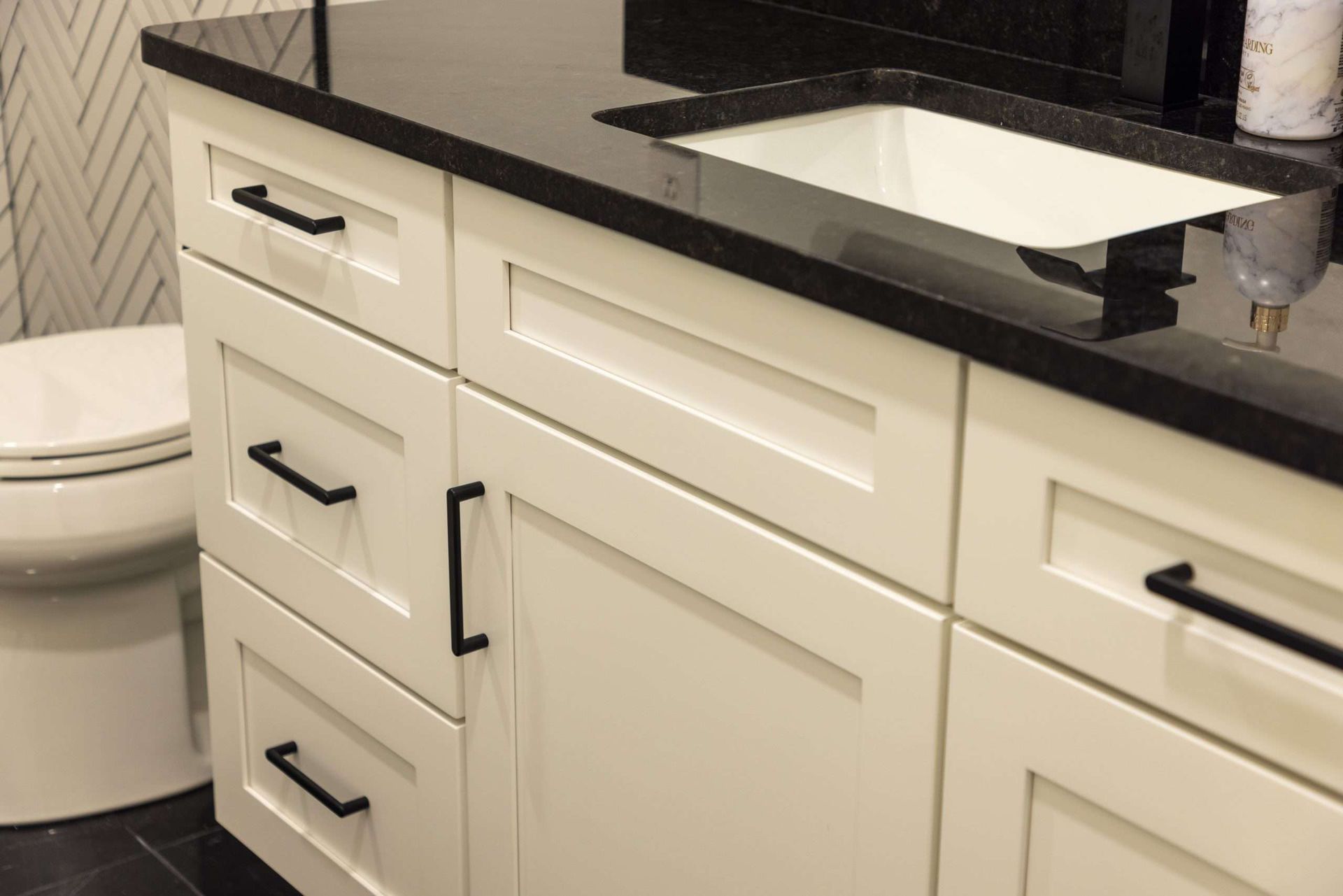 Modern bathroom vanity with white cabinets, black countertop, and sink next to a toilet