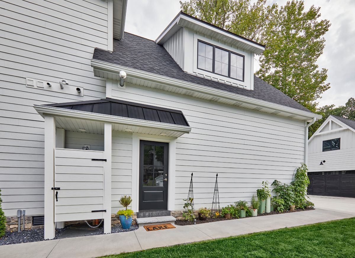 White house exterior with a front entry, dormer windows, and a small landscaped walkway
