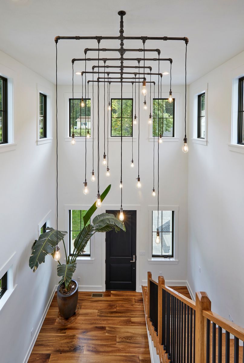 Modern stairwell with hanging pendant lights, white walls, wood steps, and large windows overlooking greenery