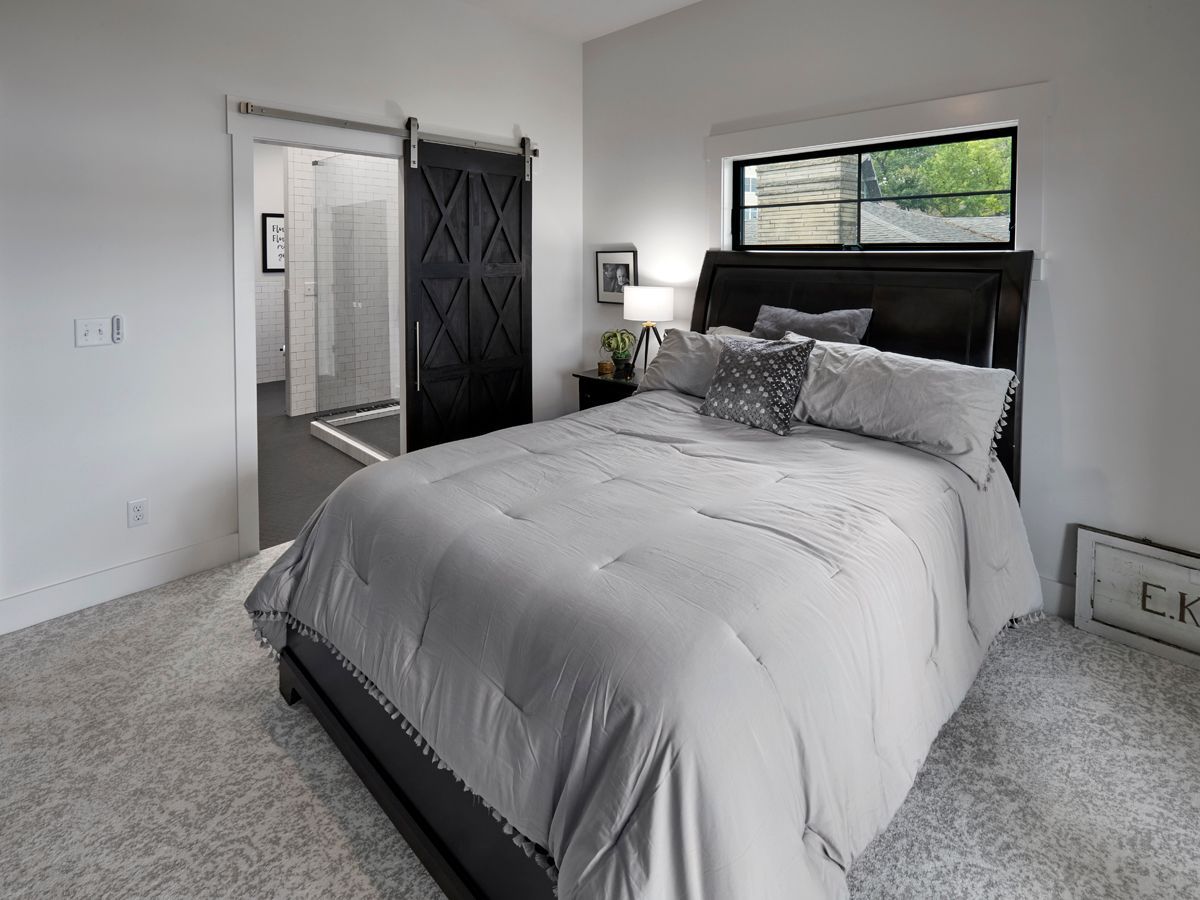 Bright bedroom with a gray bed, black headboard, and large window beside an open closet.