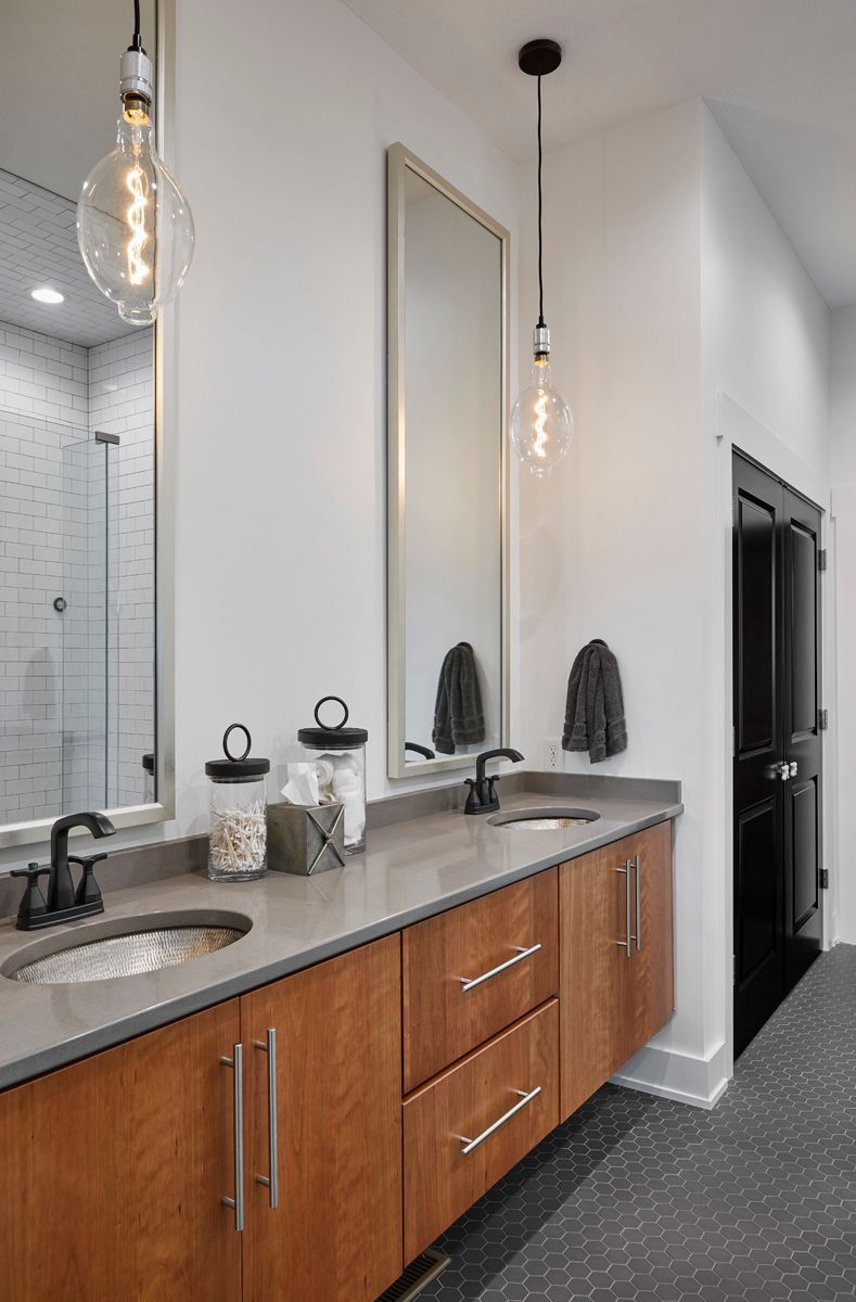 Modern bathroom vanity with double sinks, wood cabinets, large mirror, and black fixtures in a bright hallway-like space