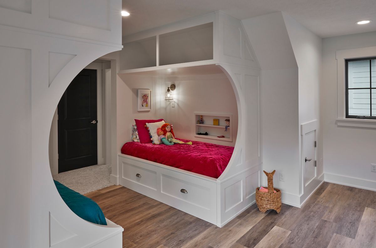 Built-in white bedroom nook with pink bedding, wood floors, and a window bench in a bright room
