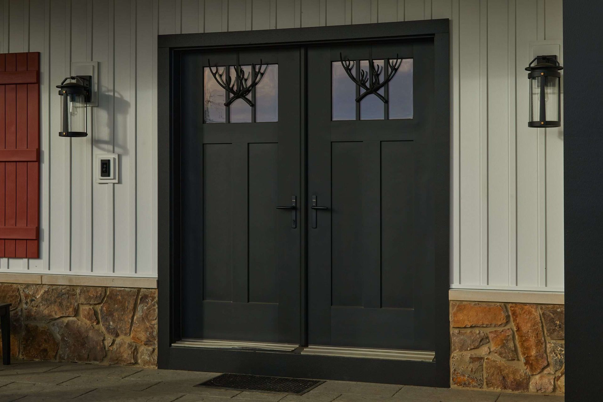 Black double doors with windows on a beige building entrance, flanked by wall lanterns.
