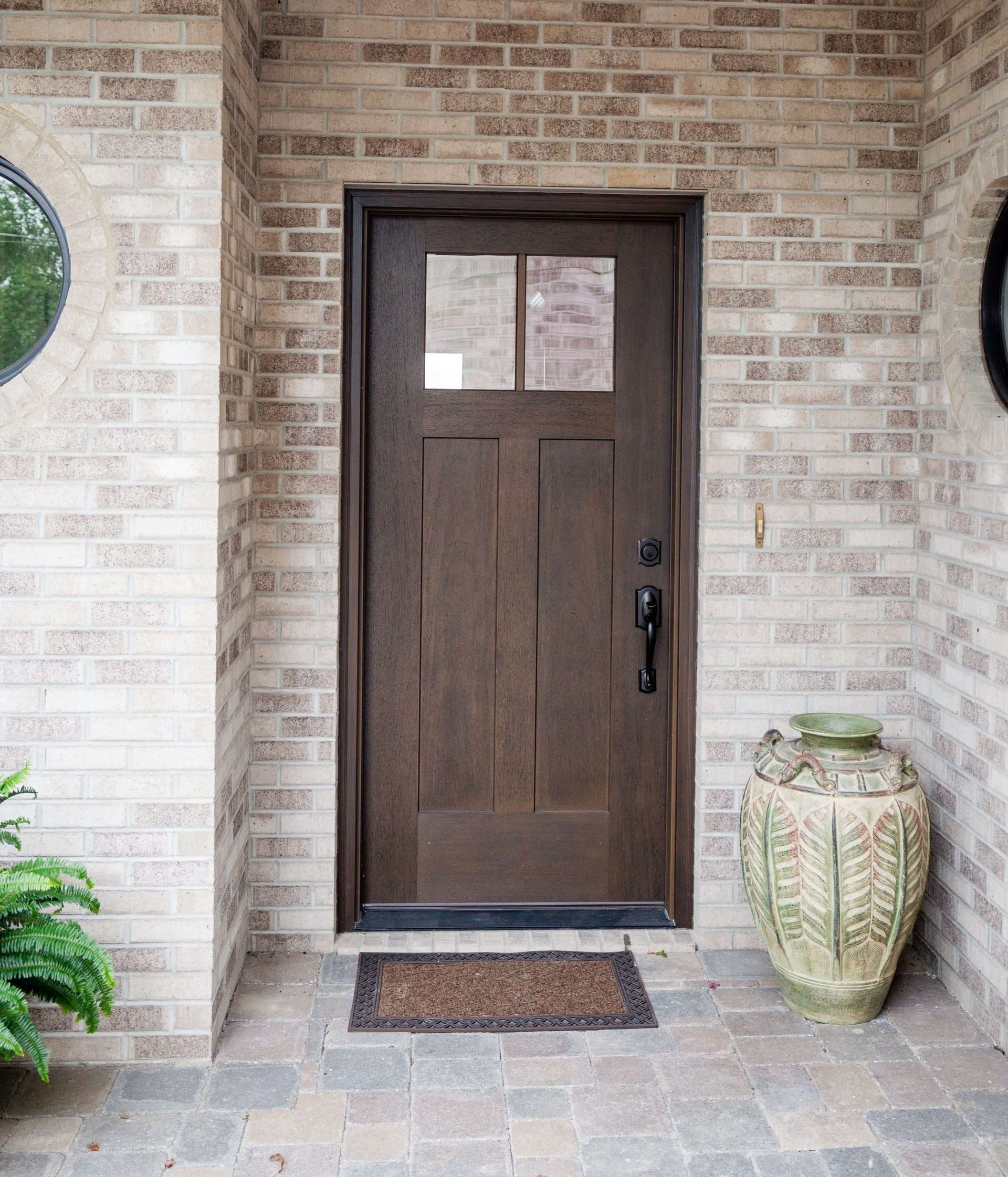 Front entrance with dark wooden door, brick walls, potted plant, and doormat.
