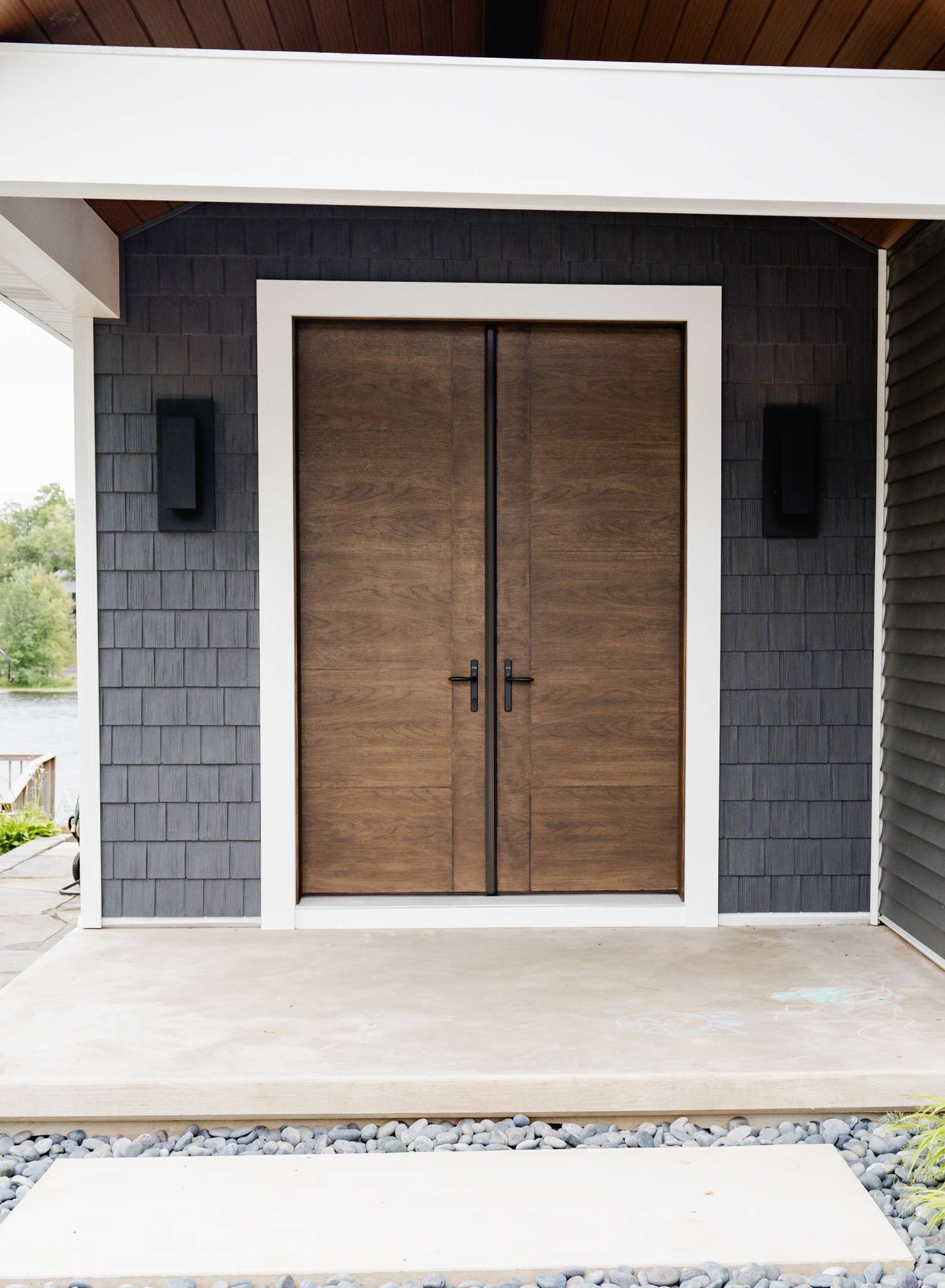 Front entry with double wooden doors in a gray stone facade and tiled porch