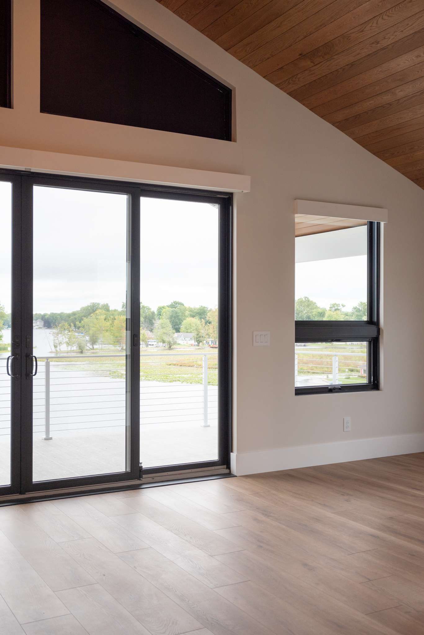 Empty modern room with vaulted wood ceiling, large sliding glass doors, and a view of water outside