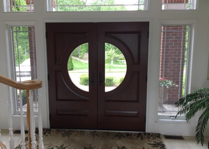 Dark wood double front doors with circular windows in a bright entryway