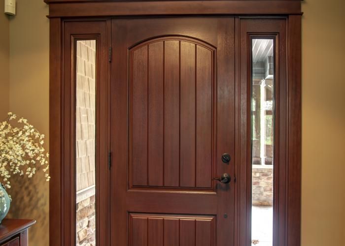 Wooden front door with glass sidelights and a dark handle in a warm entryway