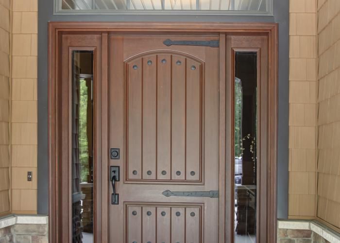 Brown front door with sidelights and arched paneling under a covered entryway