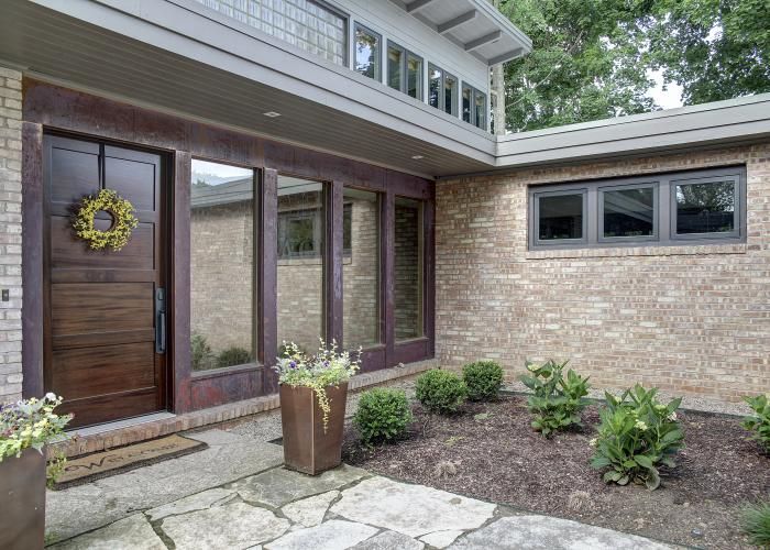 The front of a brick house with a wooden door and lots of windows.
