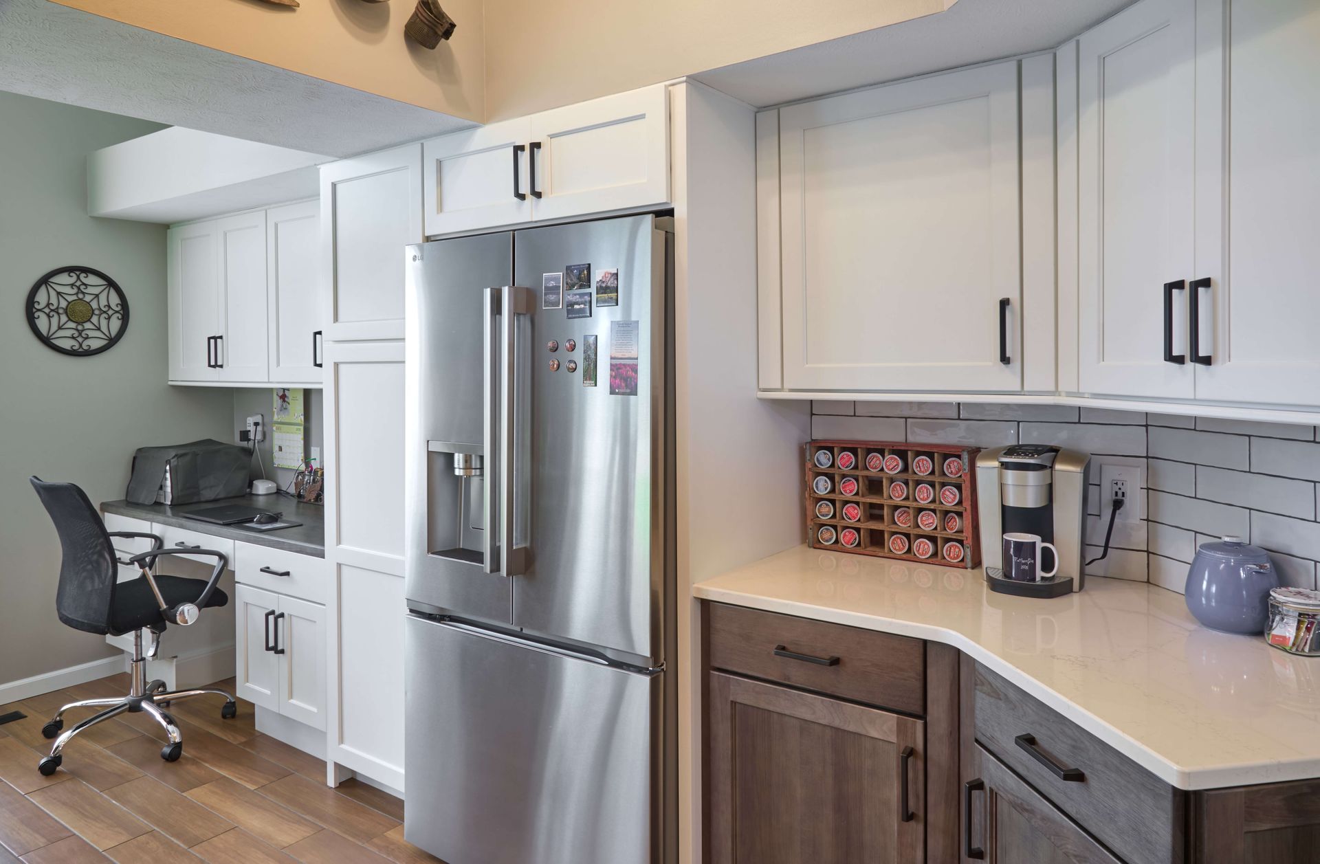 Modern white kitchen with stainless steel fridge, desk nook, and wood flooring