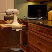 White stand mixer on a kitchen counter beside a dark wooden dresser and TV.