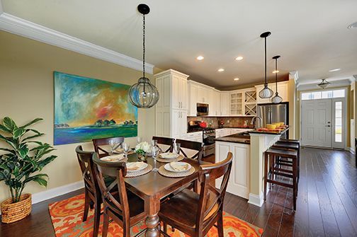 Bright dining area with wooden table, colorful artwork, and open kitchen with pendant lights