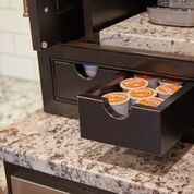 Open drawer of a coffee pod organizer on a granite countertop, showing assorted coffee pods.