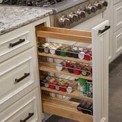 Pull-out wooden spice rack drawer in a kitchen cabinet, filled with assorted spice jars.