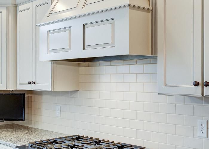 White kitchen with cabinets, subway tile backsplash, gas stove, and a range hood above the counter.