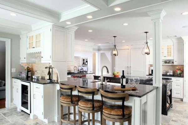 Bright white open-concept kitchen with bar stools, marble island, and hanging pendant lights