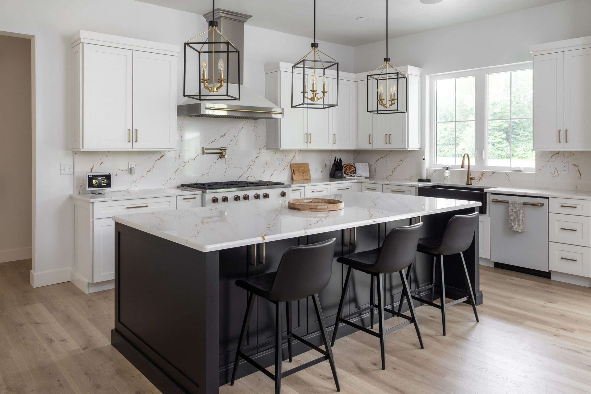 Modern white kitchen with island, black stools, pendant lights, and large windows