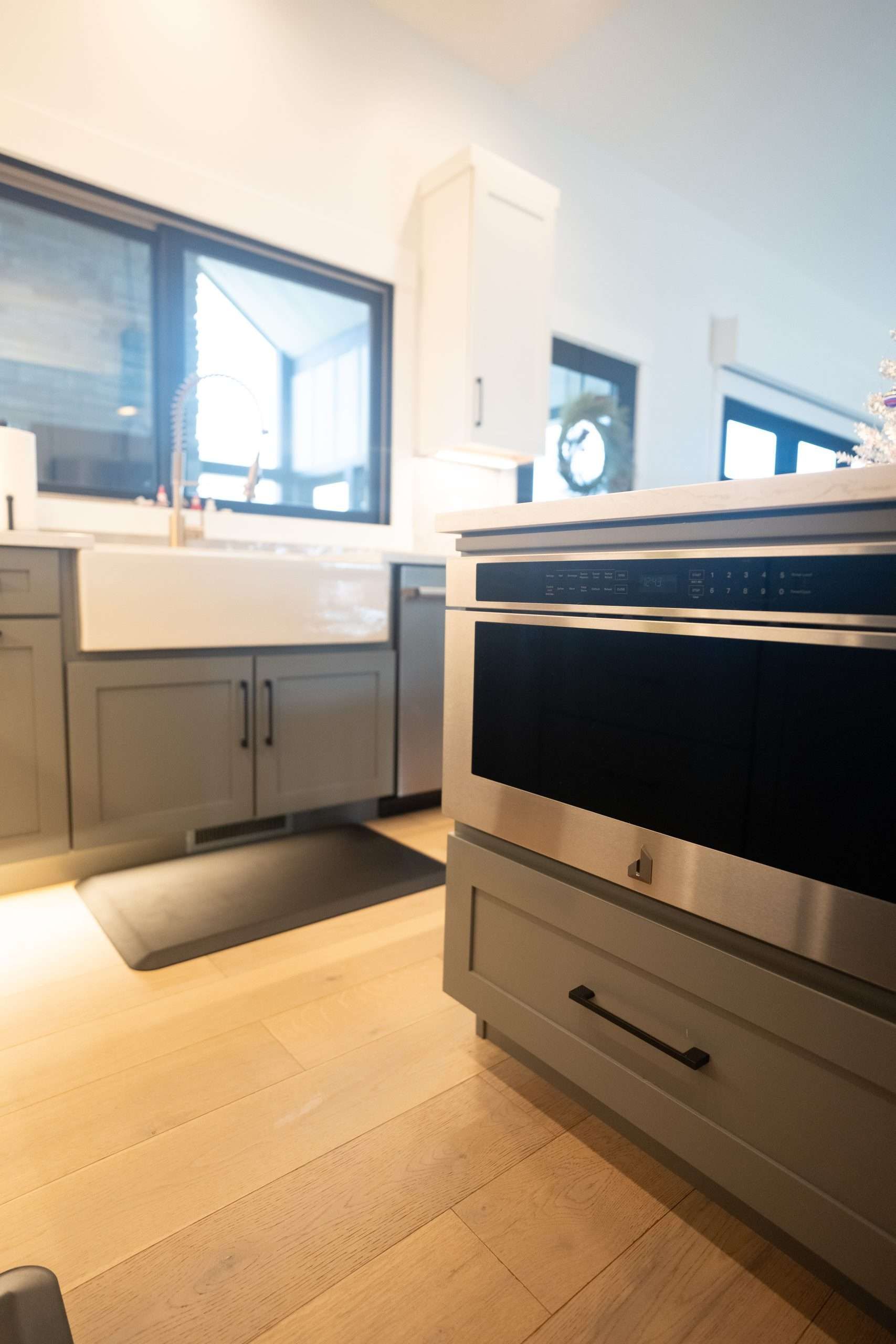 Modern kitchen with light wood floor, gray cabinets, white sink, and a stove in the foreground.