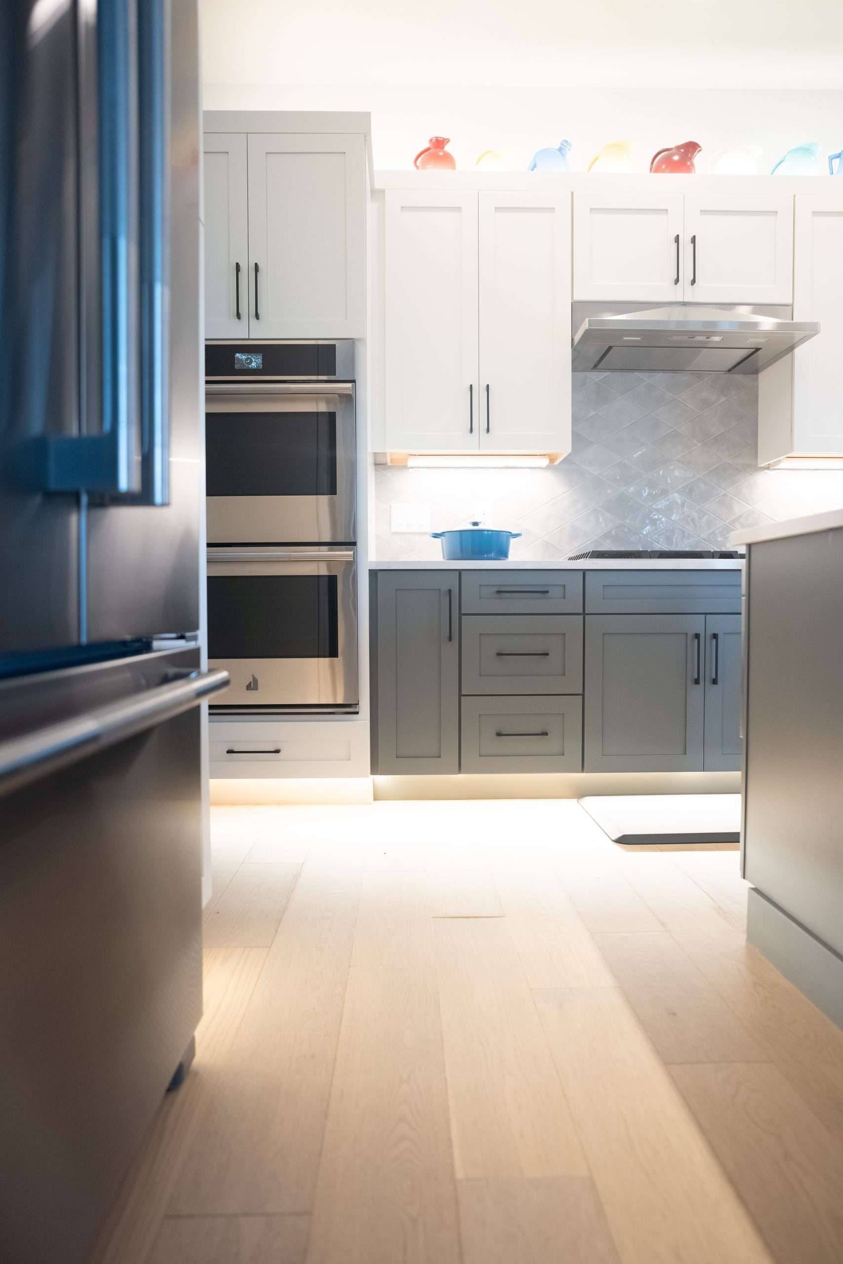 Modern white kitchen with stainless steel appliances, gray cabinets, and a bright wood floor