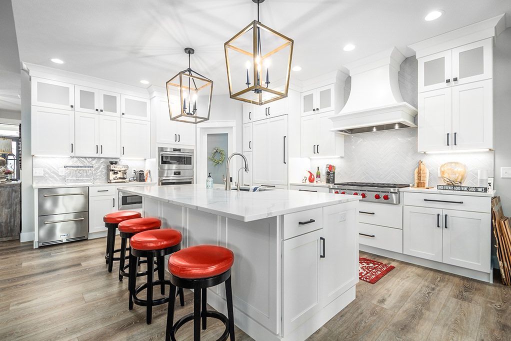 Bright white kitchen with island, red stools, pendant lights, and wood floors