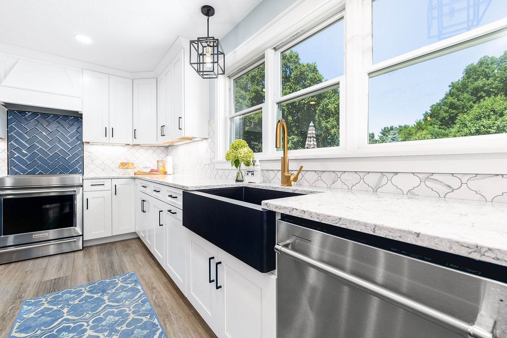 Bright white kitchen with stainless appliances, black counters, and large sunny windows.