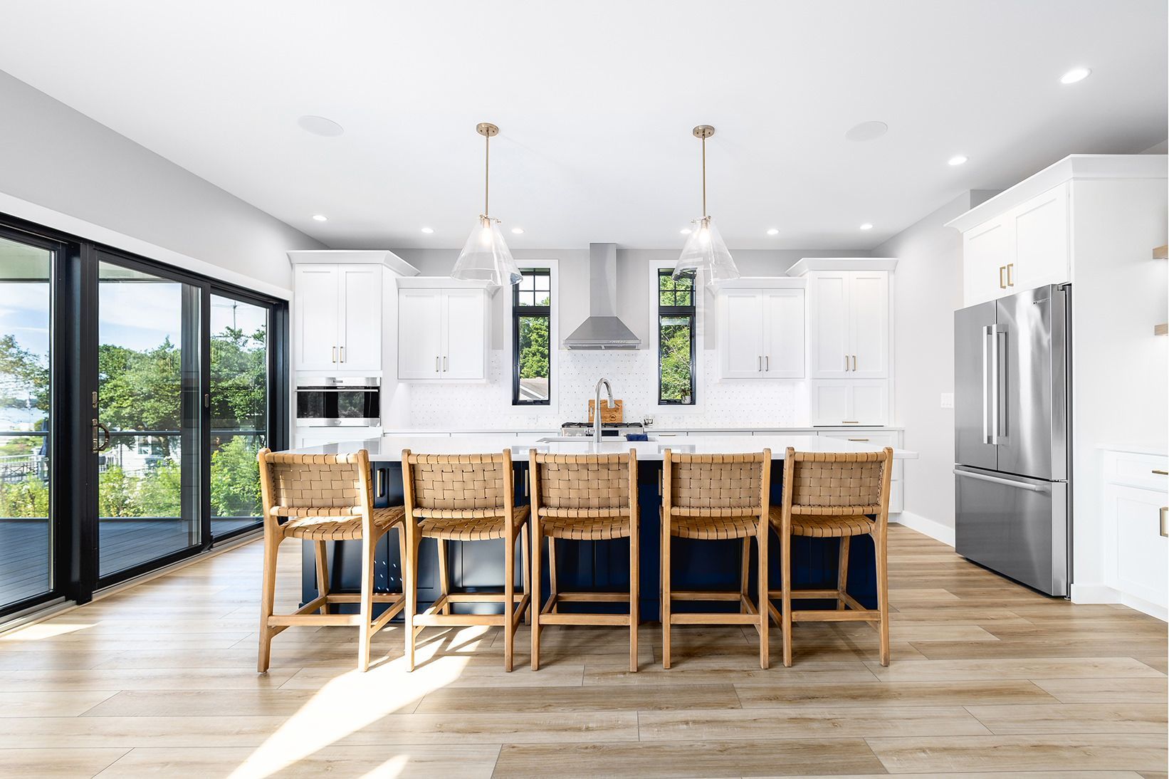 Bright modern kitchen with white cabinets, island seating, stainless steel appliances, and large sliding glass doors