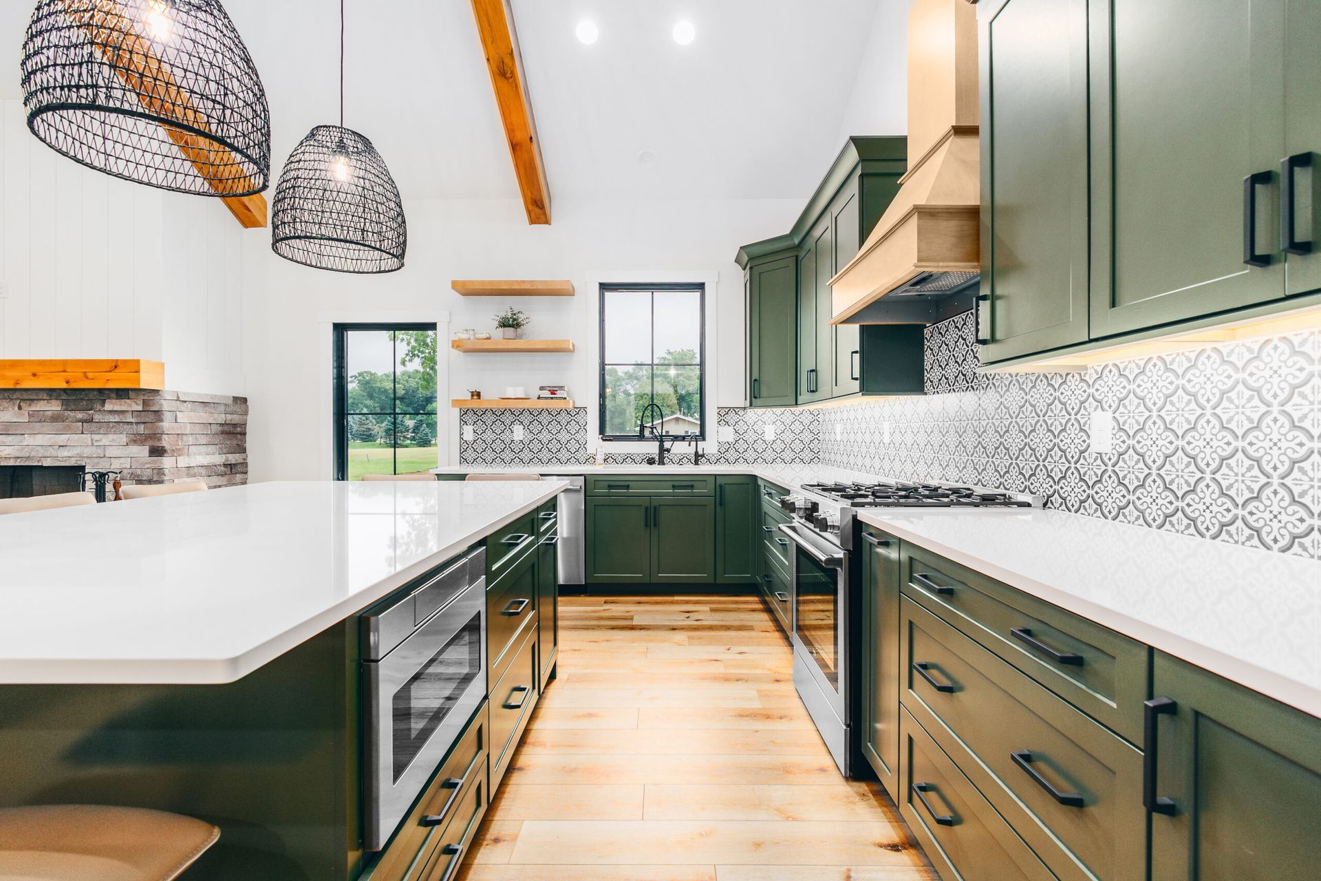 Modern kitchen with green cabinets, white island, woven pendant lights, and herringbone wood floor