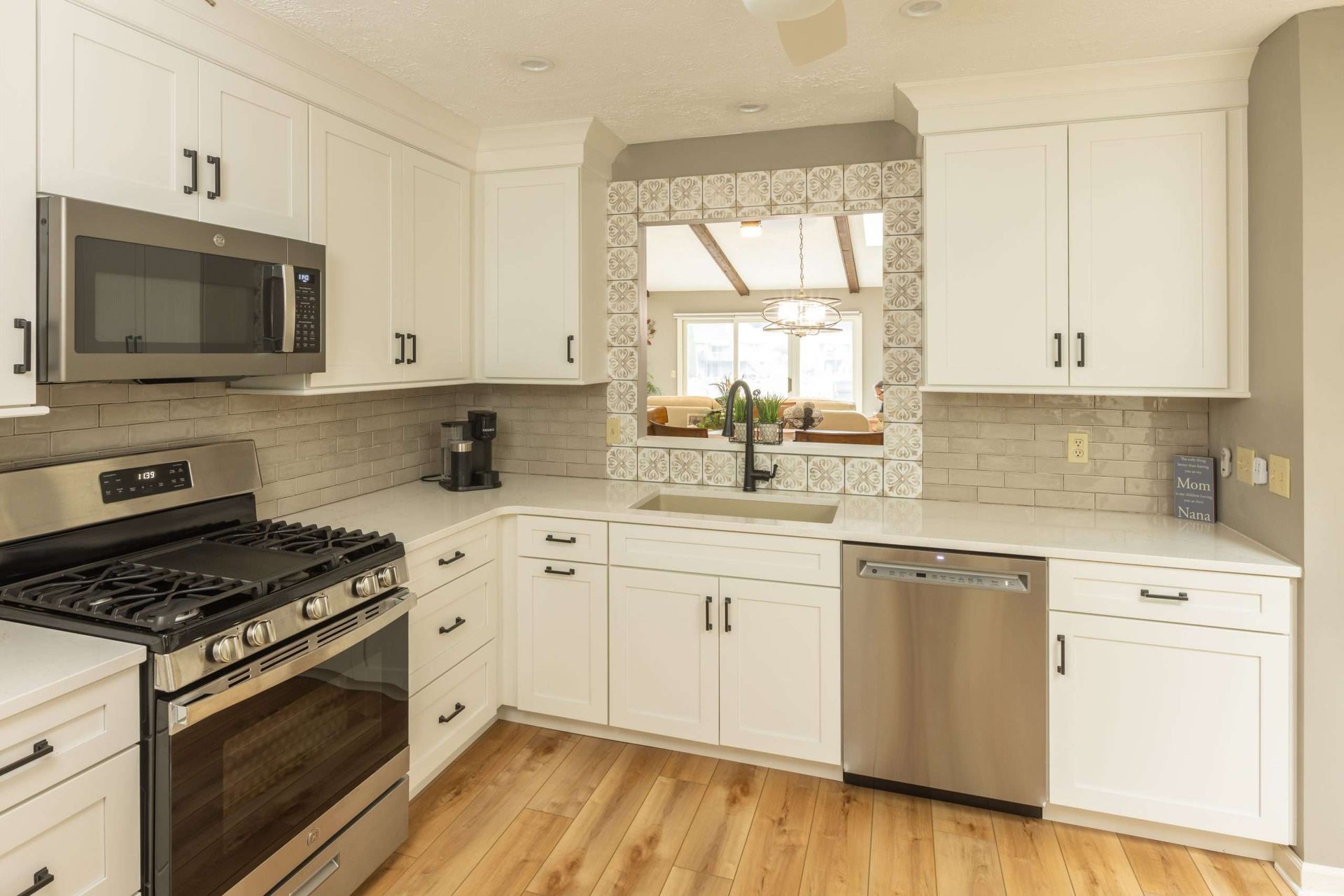 Bright white kitchen with stainless steel appliances, wood floor, and window over the sink