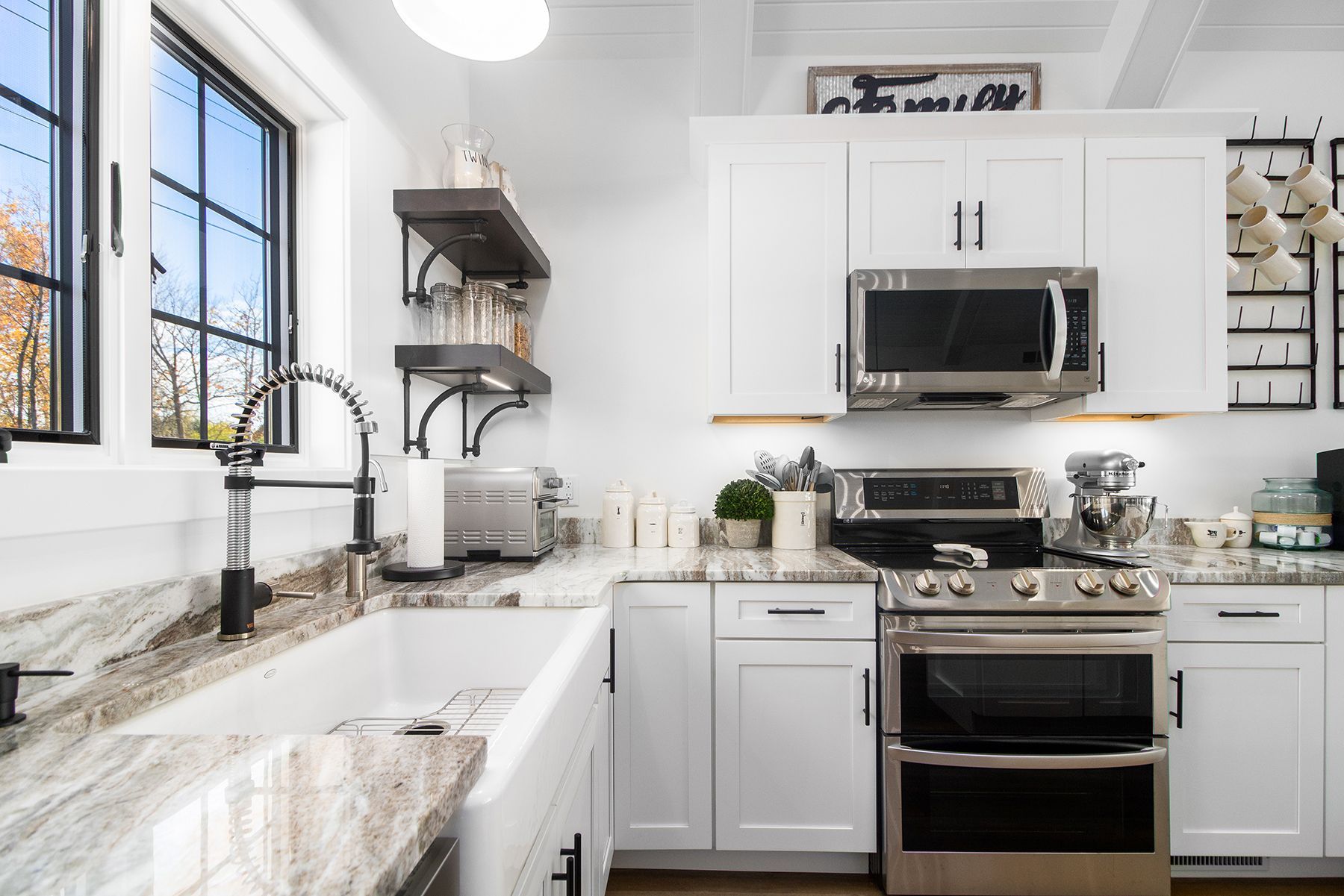 Bright white kitchen with marble counters, farmhouse sink, black stove, and microwave above it
